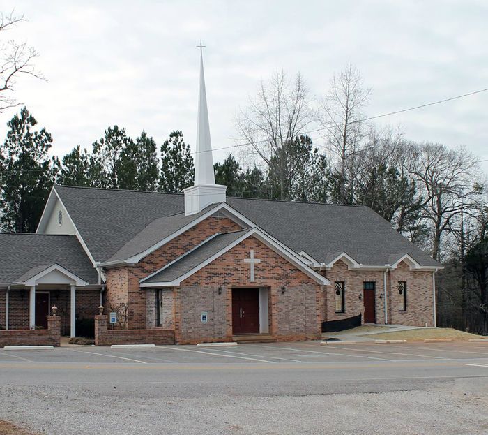 This is Red Ridge United Methodist Church at the intersection of Alabama Highway 49 and Tallapoosa County Road 34. Stories about Red Ridge date back to the Civil War and before.  Early historians indicated that the first church was a log structure located west of the Dadeville-Tallassee Highway (now identified as Highway 49).  The name of that church was Salem and was on a site near the cemetery located just inside the Highway 34 gate of Stillwaters.  This building burned. The second structure, a wooded and weather board structure, was constructed on a site east of the Dadeville-Tallassee Highway in the early 1850’s near the present structure.  This was in the Beat 9 voting precinct, which was called Red Ridge, thus the name of the community and the church. In 1892 the Agricola church was built and some people left Red Ridge and went to the new church.  However, Red Ridge survived this split and remained a vital part of the community, at times few in number, but strong in faith.  Red Ridge Methodist Church, in 1909, was not a part of the Conference for a short while; however, due to appeals by Rev. J. A. Smith and others, the church was accepted back into the North Alabama Conference.
In its present location, the original sanctuary was partly constructed around 1925 including hand-hewn sills from the old church. Picture in your mind the plain rectangular wooden building painted white on the outside, no porch but two steps up to the two front doors opening directly into the sanctuary.  Two plain windows behind the altar and along each side three plain windows.  Plain wide plank homemade wooden pews, a potbelly wood burning stove in the middle of the floor, brackets for kerosene lamps along the walls and an old-time pump organ in the corner for music.  In the late 1930’s and early 1940’s, Red Ridge was on a charge with Flint Hill, Poplar Springs, Agricola, and Macedonia.  (I cannot locate Macedonia, but I think it was Buttston.)  During this time, worship services were held once each month, sometimes on Sunday afternoon, but Sunday School was every Sunday.  About this time electricity came to the area and two drop-cord lights provided an abundance of light.  The church also acquired an up-right piano about this time.  Agricola Church was officially disbanded about 1949-1950.  When this happened the Conference gave Red Ridge anything usable from the church since it was falling down.  The pews, pulpit and spindles in our altar rail came from Agricola.
As you can see, many changes have taken place – electricity, carpet, pew pads, central heat and air, stained glass windows, indoor bathroom, brick work on the outside and the steeple.  It was erected in 1987 and dedicated on May 17th of that year.  A new sound system, additional parking, a new piano and organ have been added as well.  Also, a sanctuary addition has been completed in the last few years.
Worship services have changed from one Sunday per month to two Sundays to every Sunday.  Since 1974 when we were paired with Camp Hill our worship service has been at 9:30 a.m. and it was between 1983-1985 when weekly worship services began.   Membership has fluctuated through the years from 70+ in 1937, down to 35-40 in the 1950’s and 1960’s, with attendance at about 12-15 per Sunday.  Currently membership is about 239 and attendance is approximately 135 each Sunday.  I was writing this history October 13, 2002 after the Board meeting at which we approved a budget for 2003 of over $100,000.00.  In my folder of research data on Red Ridge United Methodist Church I found a copy of the 1952-1953 budget (50 years old).  The total was $691.80.  Yes, $691.80 for the entire year.  Times have changed.  Thanks to all of those who have worked so hard through the years to keep Red Ridge United Methodist Church a vital part of this area. It seems that a church  building has been at this location since the early 1850's. By Ruth Lockett in 2002